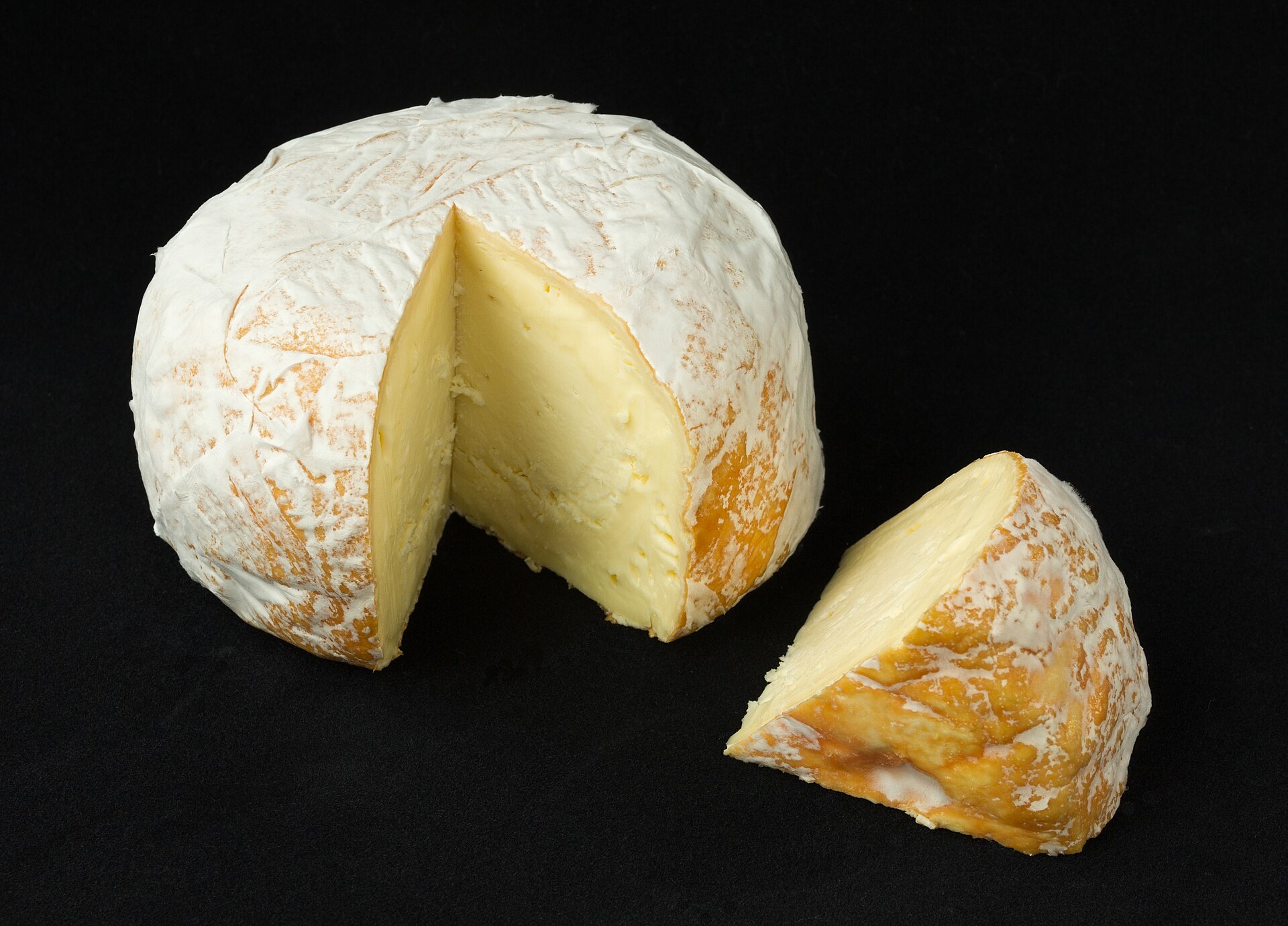 Soft bloomy-rind cheese wheel with a wedge cut out