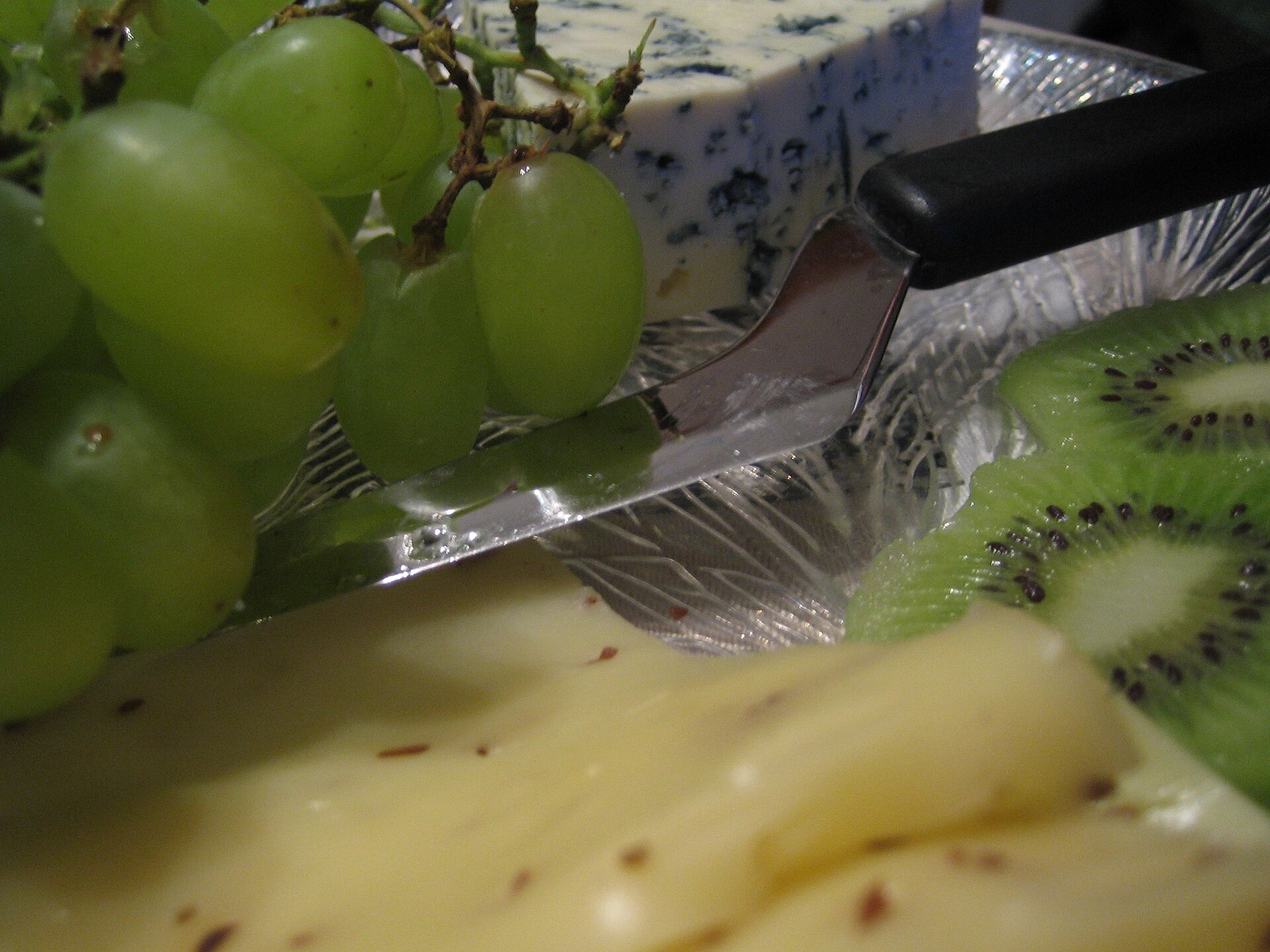 Cheese, grapes, and kiwi served on a glass plate with a cheese knife